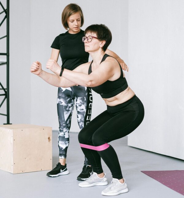 Woman in Black Sports Bra and Leggings Doing Exercise with Personal Trainer